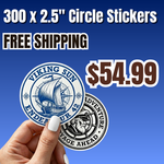 Promotional offer for 300 custom 2.5 inch circle vinyl stickers for $54.99 with free shipping. A hand displays two round die-cut stickers with vintage nautical ship and badge artwork in blue and black under clean studio lighting. Ideal for e-commerce product display and bulk orders.