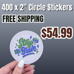 Promotional banner for “400 custom 2 inch circle vinyl stickers for $54.99 with free shipping”. A hand holds a round waterproof decal featuring “Stay Brave” typography with green and blue graphics and camera icons, showcasing high-quality custom vinyl stickers ideal for bulk sticker printing and branding.