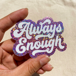 Hand holding a 'Always Enough' glitter sticker against a beige background