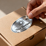 Hand placing a 'Nice Boutique' silver sticker on a cardboard box for packaging