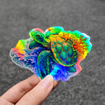 Colorful turtle and coral holographic sticker held by a hand against a dark background