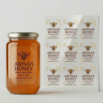 Custom clear labels on a glass honey jar next to a printed sticker sheet, showcasing transparent product labels with gold honeycomb designs.