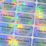 Custom holographic vinyl labels with rainbow foil finish. These die-cut stickers feature a decorative border and black ink printing, showing off the iridescent color shift and premium texture.