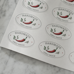 Custom oval sheet labels for handmade chili sauce packaging, featuring white product stickers with pepper artwork arranged on sheets