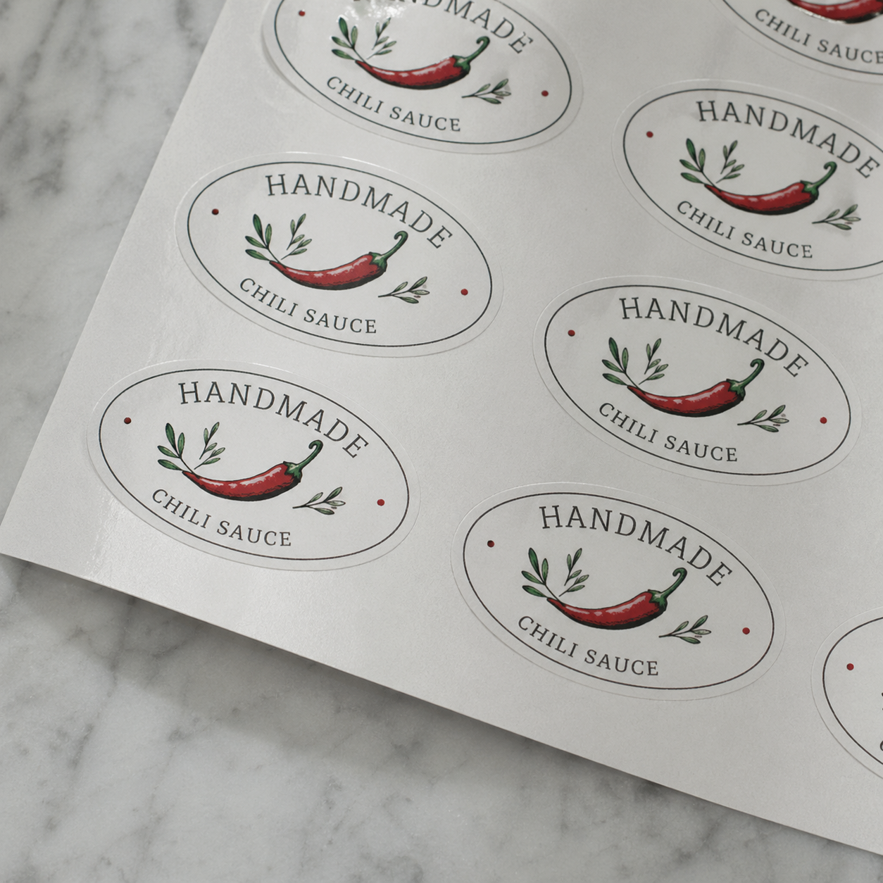 Custom oval sheet labels for handmade chili sauce packaging, featuring white product stickers with pepper artwork arranged on sheets