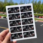 Custom rounded corner sheet labels for racing team stickers, shown on a printed sheet held outdoors near a race track