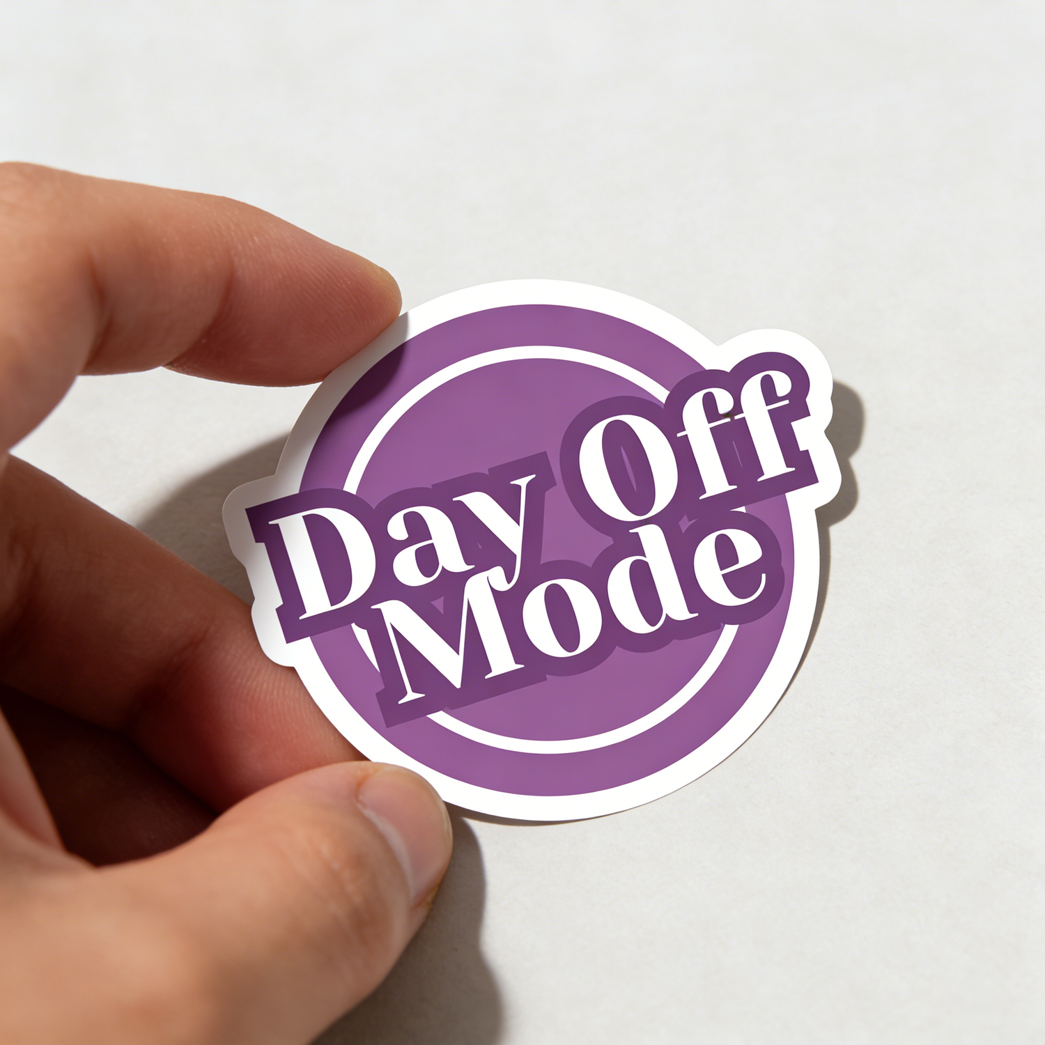 Hand holding a purple 'Day Off Mode' vinyl sticker against a white background, waterproof and UV-resistant