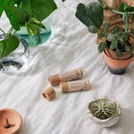 Two brown cylindrical products labeled 'Gentle Care' custom printed lip balm labels​ on a white fabric background with plants.