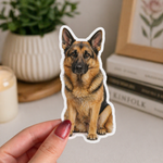 Hand holding a German Shepherd pet dog sticker on a neutral background with decor elements.