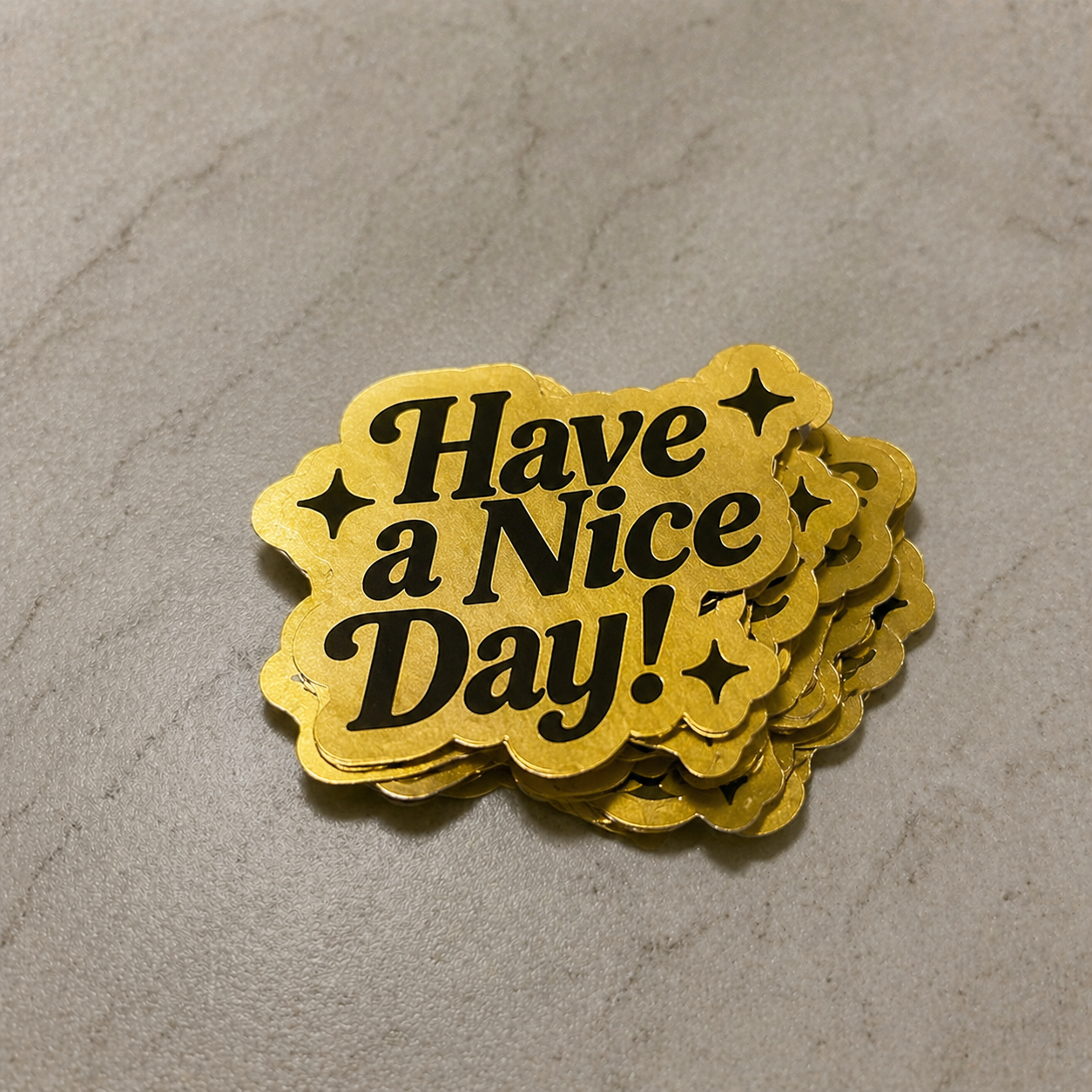 Stack of gold stickers with 'Have a Nice Day!' text on a gray surface