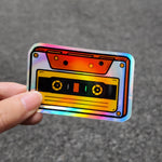 Holographic sticker of a cassette tape held by a hand on a gray background