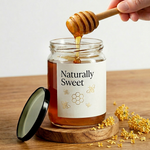 Honey being drizzled from a wooden dipper into a jar labeled 'Naturally Sweet' on a wooden surface.