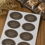 Oval sheet labels for handmade cookie packaging, featuring brown bakery stickers printed on sheets beside wrapped cookies and a cooling rack