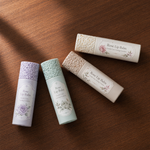 Four tube rose lip balms with logo labels​ on a wooden surface
