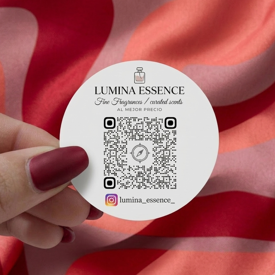 Round QR code sticker with Lumina Essence branding held by a hand against a red and pink striped background, including logo and Instagram handle for fragrance brand promotion
