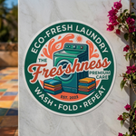 Round outdoor decal for "Eco-Fresh Laundry" featuring a washing machine illustration and "Wash, Fold, Repeat" text, applied to a white marble outdoor wall.