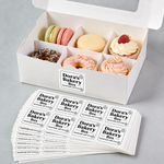 Box of assorted pastries with 'Dora's Bakery Box' Rounded corner sheet labels on a gray background