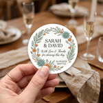 Round sticker with custom names "Sarah & David“ and wedding date ”24.09.2023“ used as wedding favor over a decorated table.
