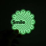 Glowing green 'Smile' sticker held against a dark background