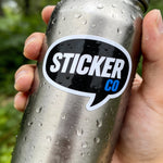Metallic water bottle with a 'Sticker Co' sticker held by a hand against a blurred green background