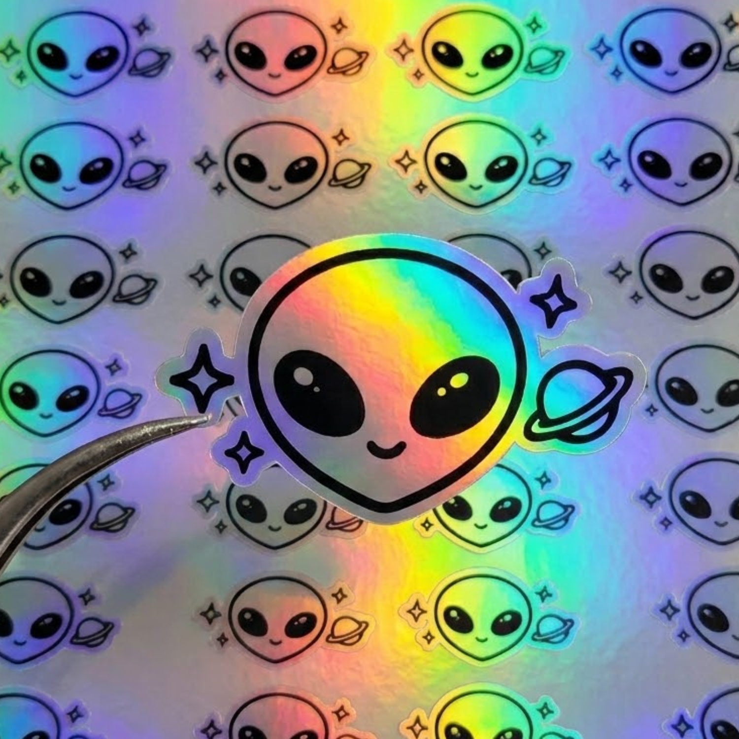 Tweezers peeling a custom kiss-cut alien holographic label from an easy-peel sheet, demonstrating how to make holographic labels easy to apply.