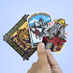 Hand holding a variety of custom vinyl stickers featuring leopard, alpine ascent, and DJ skeleton designs.