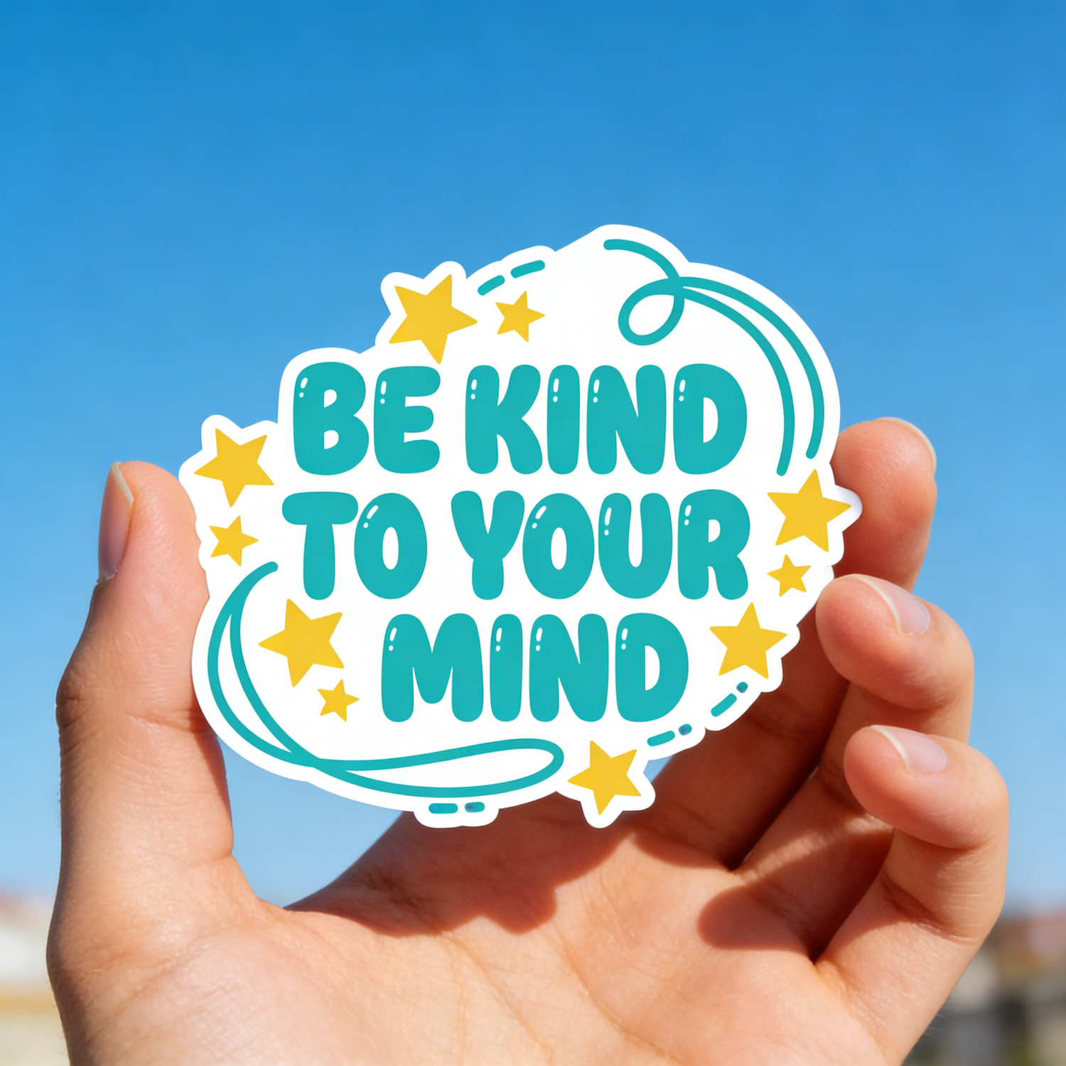 Hand holding a sticker with 'Be kind to your mind' text against a blue sky.