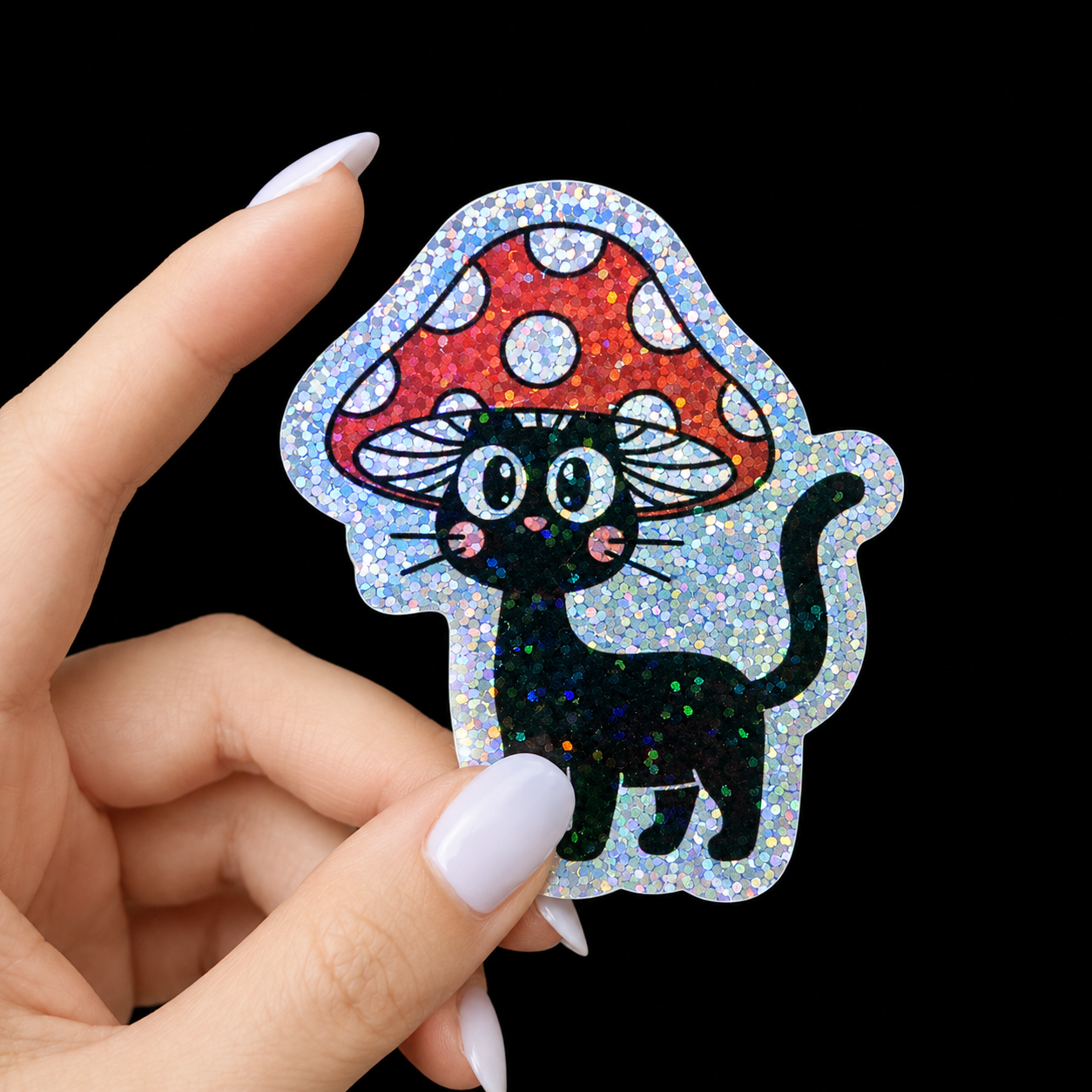 Hand holding a glittery sticker of a black cat under a red mushroom with white spots on a black background.
