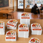 Multiple stacks of custom Fresh Slice Pizza safety seal stickers on a wooden table.