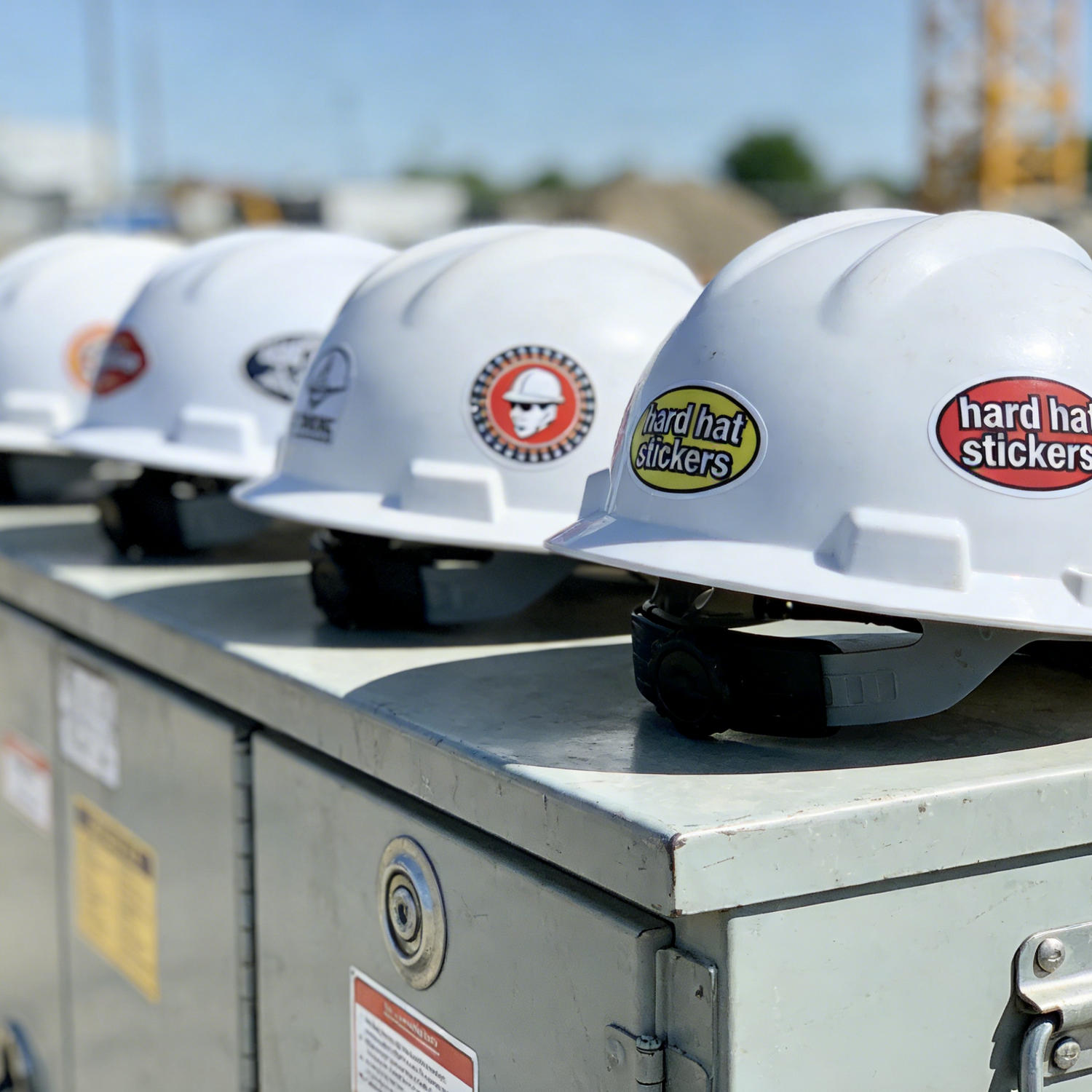 White hard hats with a variety of cool and personalized stickers on a metal surface at a construction site.