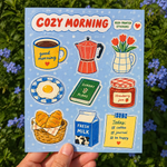 Sticker sheet featuring watercolor illustrations of a coffee cup, moka pot, tulip vase, fried egg, planner, strawberry jam, croissants, milk carton, and a to-do note on a light blue background.