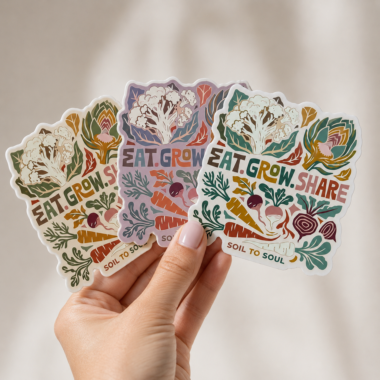 Hand holding three colorful stickers with vegetable illustrations Eat Grow Share artist stickers on a neutral background