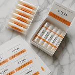 Custom citrus lip balm labels on sheets next to labeled lip balm tubes in packaging boxes.