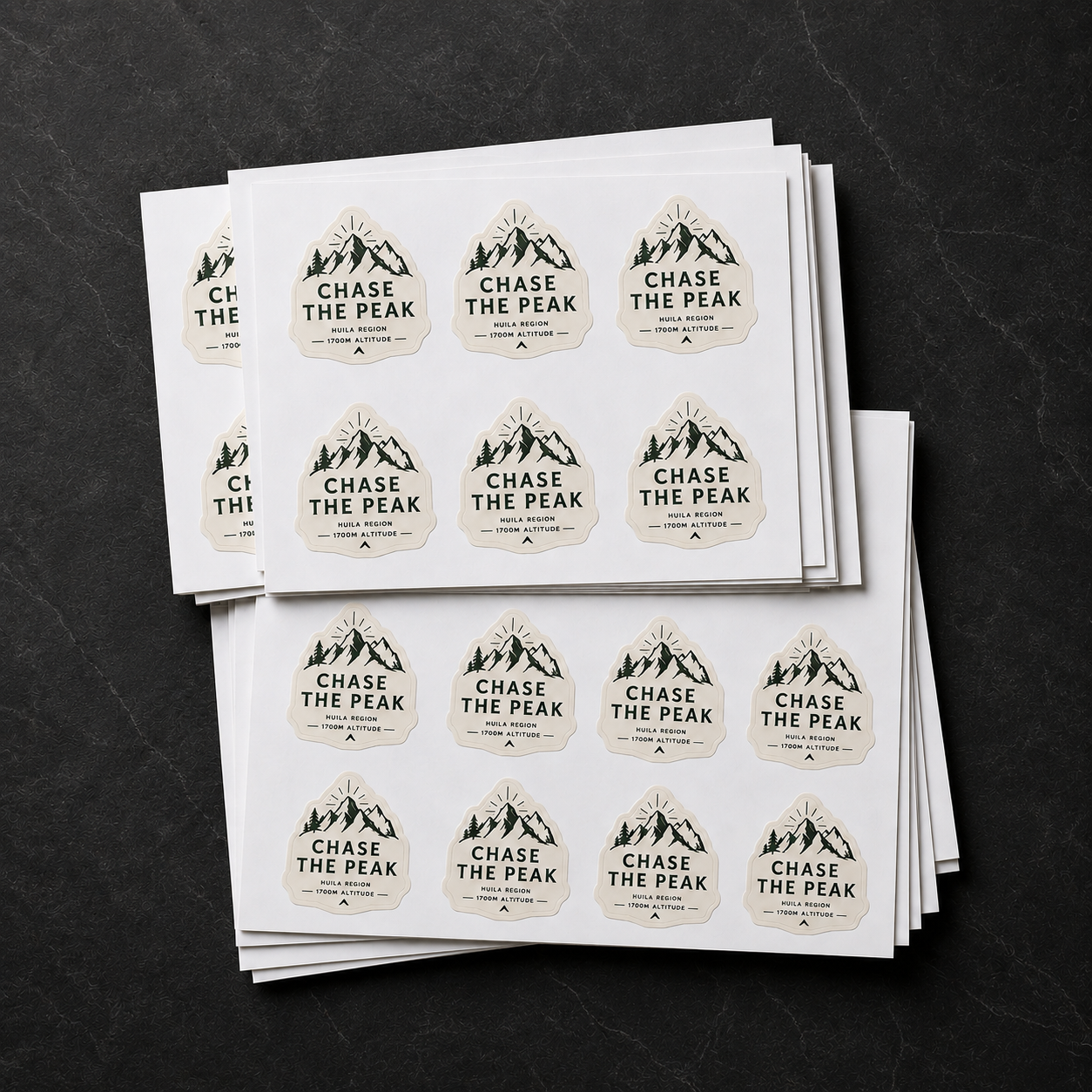 Stack of custom die-cut vinyl label sheets featuring a mountain design for Chase The Peak coffee brand, showcasing premium waterproof vinyl stickers on a dark textured background.