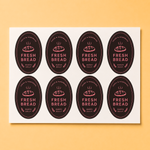 Custom oval-shaped vinyl labels with Fresh Bread branding displayed on a sticker sheet.