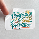 A close-up of a high-quality glossy sticker with "Progress Over Perfection" text being peeled off a smooth white surface.