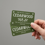 Hand holding two green rounded corner stickers with 'Cedarwood' branding against a gray background