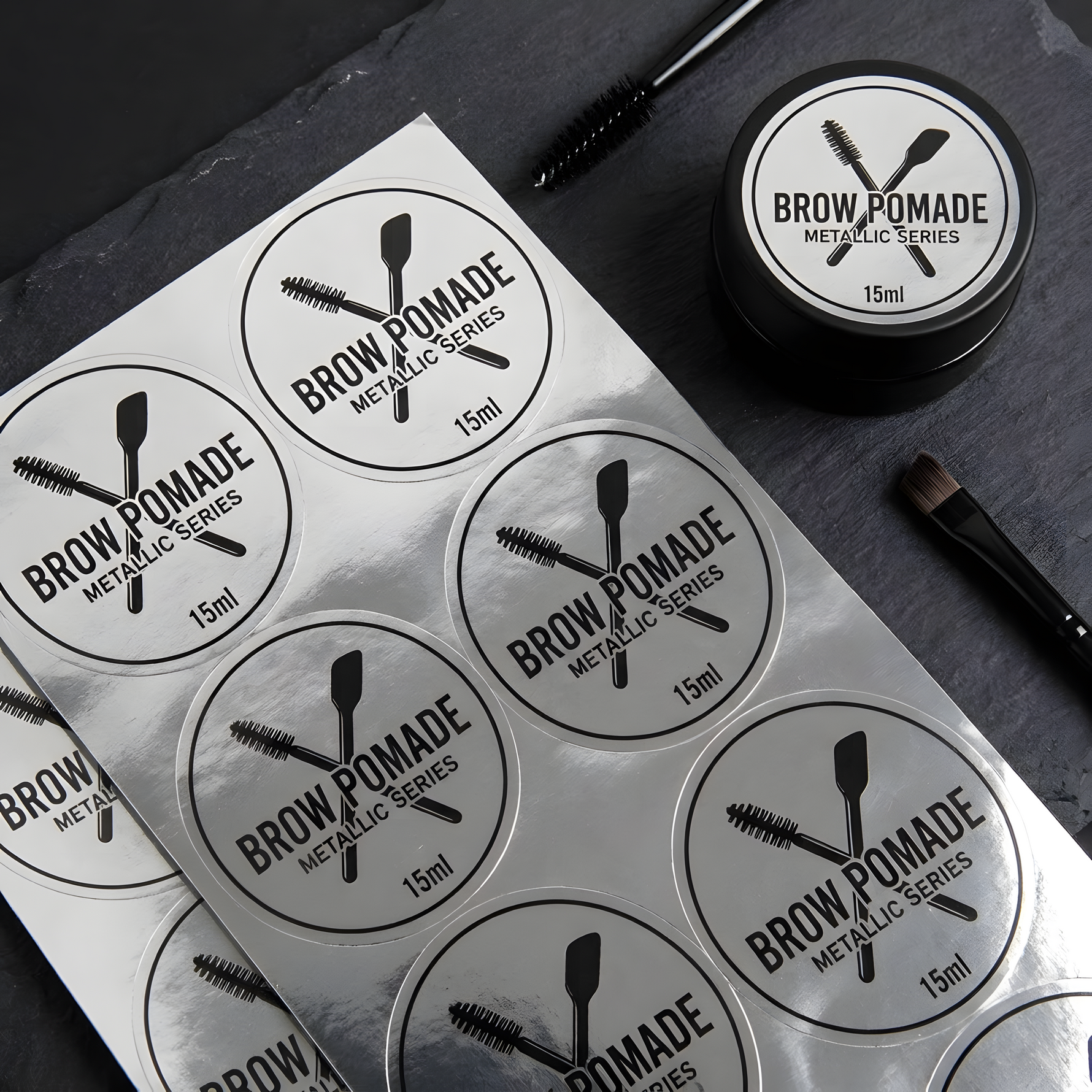 Custom metallic silver labels shown on a brow pomade container and matching round label sheets.