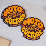 Custom die-cut motorcycle logo stickers with an orange Moto Culture design displayed on a wooden table.