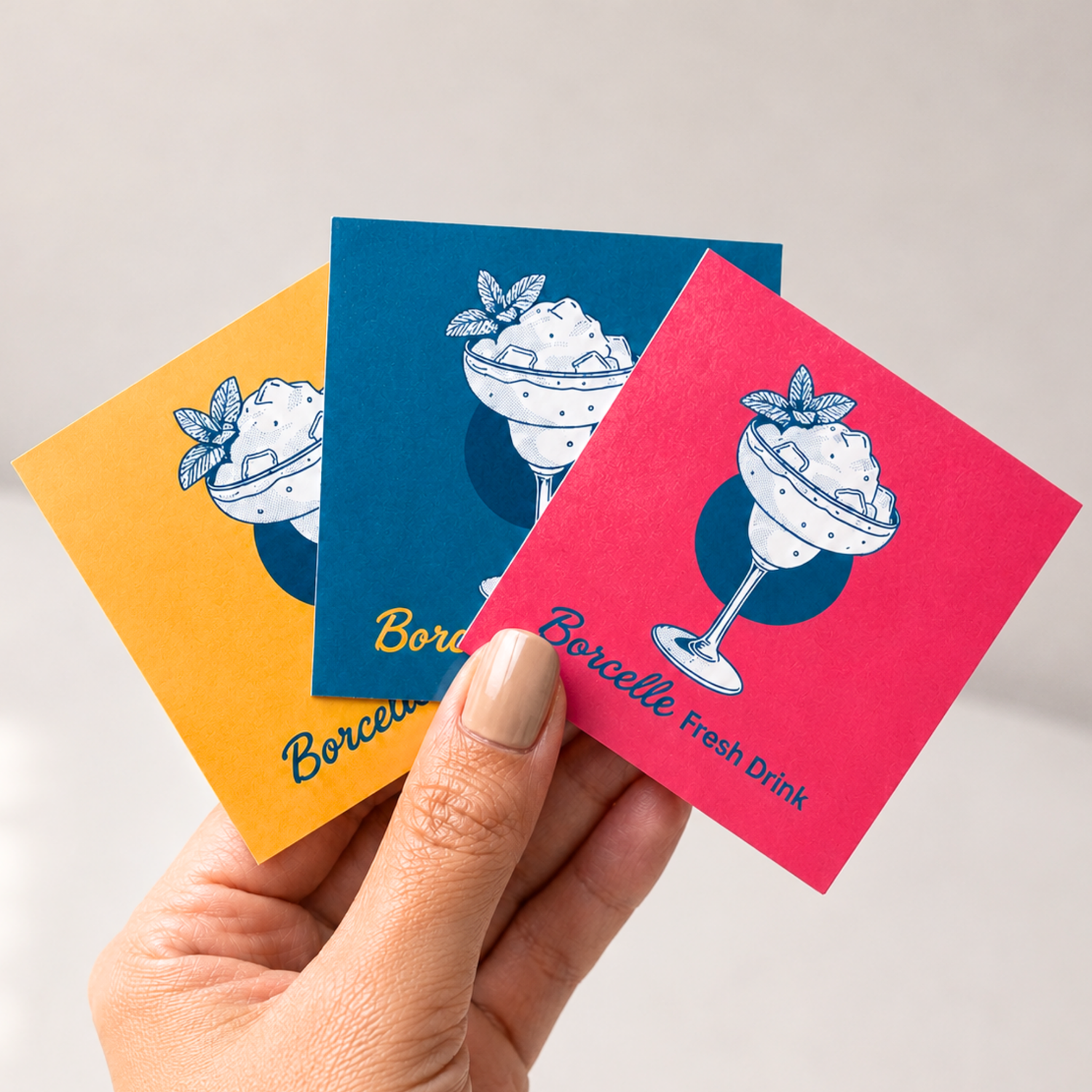 Hand holding three colorful custom square stickers with fresh drink illustrations, logo stickers for brand promotion