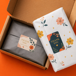 Two custom rectangular business packaging stickers with 'Thank You' text sealing grey and floral tissue paper inside a brown mailer box.