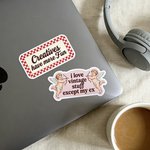 Two high-definition custom vinyl stickers placed on a silver laptop next to headphones and a coffee cup, featuring a red checkered 'Creatives have more Fun' sticker and a vintage cupid 'i love vintage stuff except my ex' sticker.