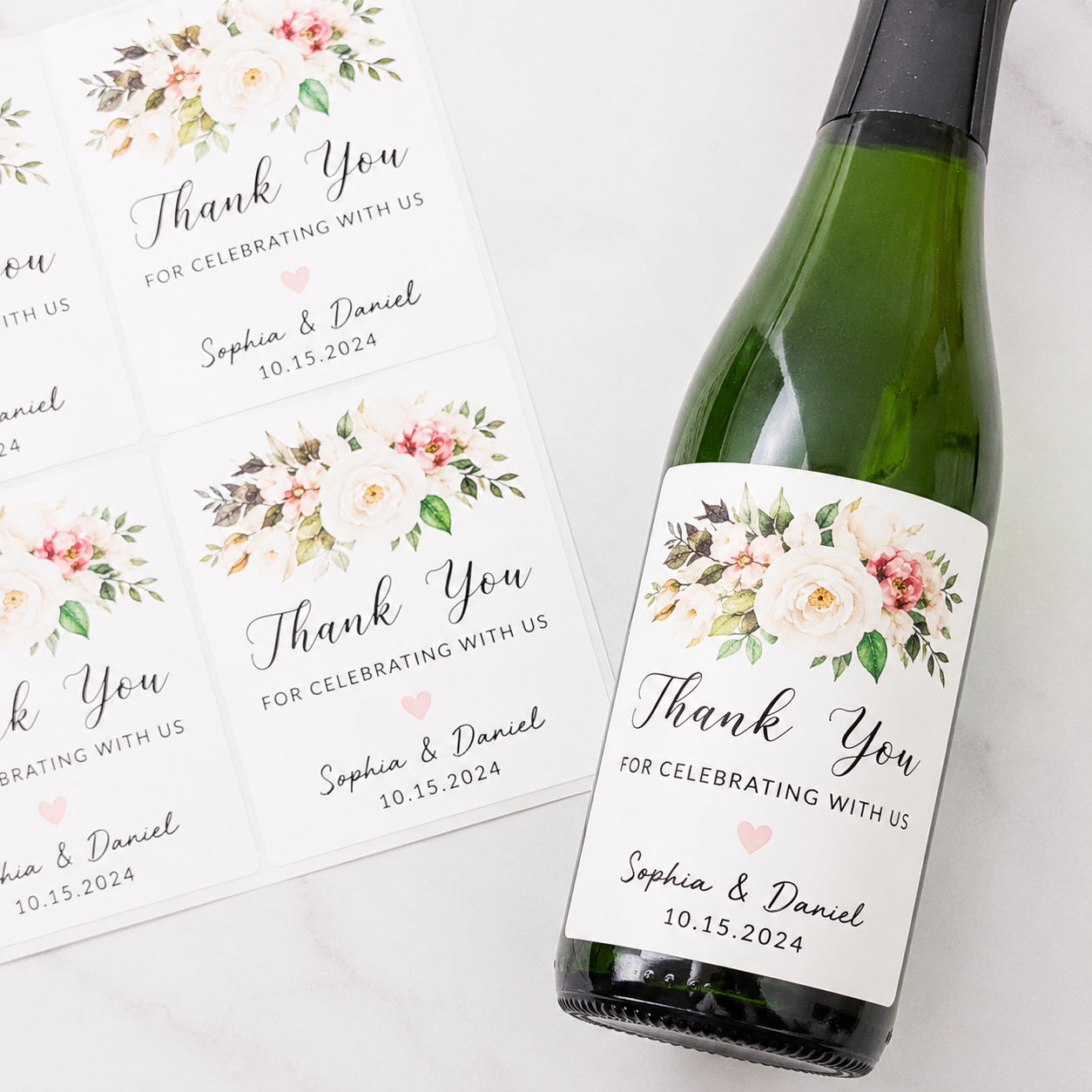 Personalized wedding thank you wine labels with a delicate white and pink floral bouquet design, featuring the names "Sophia & Daniel" and the wedding date, shown on a green wine bottle and a sticker sheet.