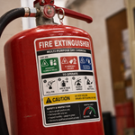 Close-up of a permanent vinyl safety label on a red fire extinguisher, showing clear operating instructions and safety classifications for industrial use.