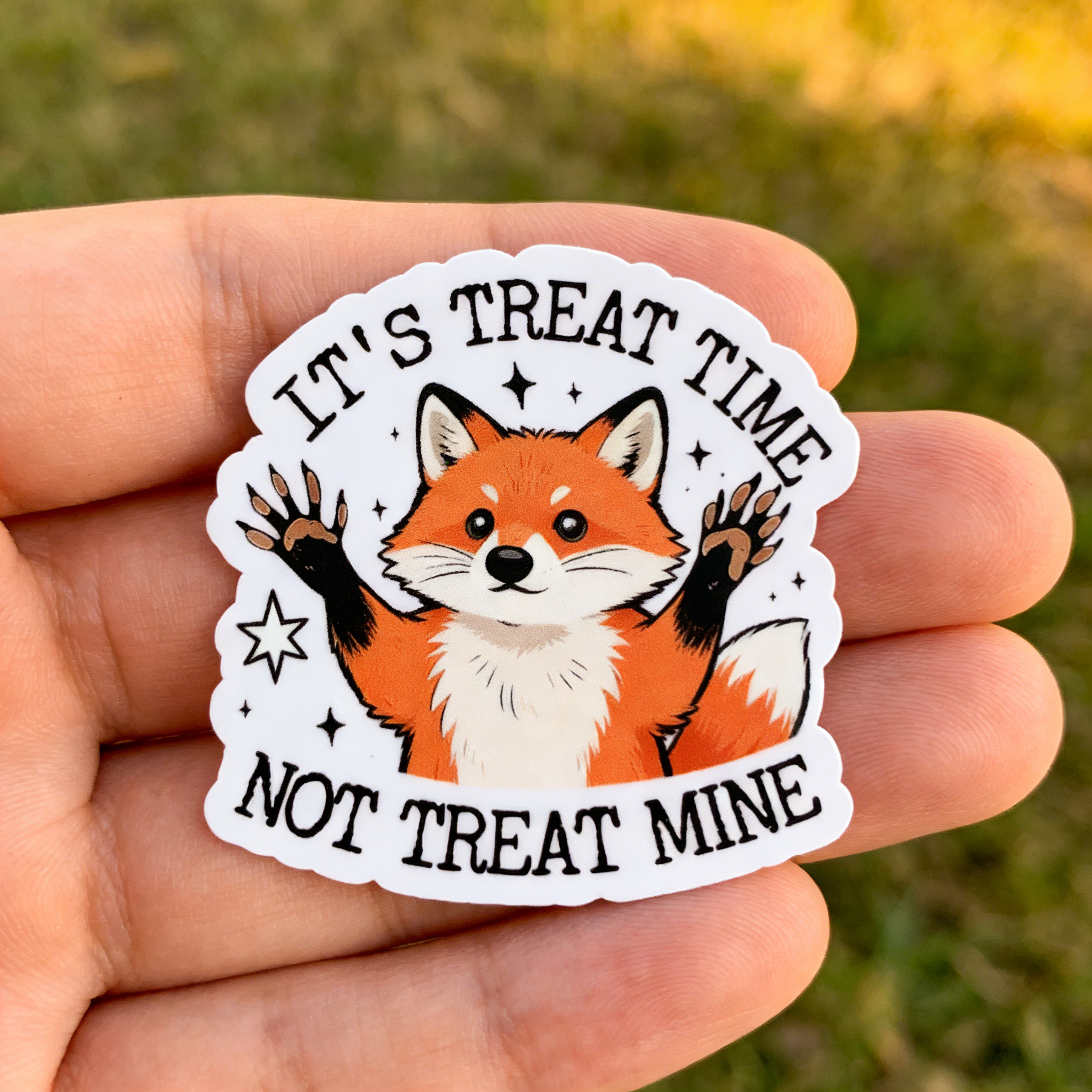 Sticker with a fox design held in a hand against a grassy background