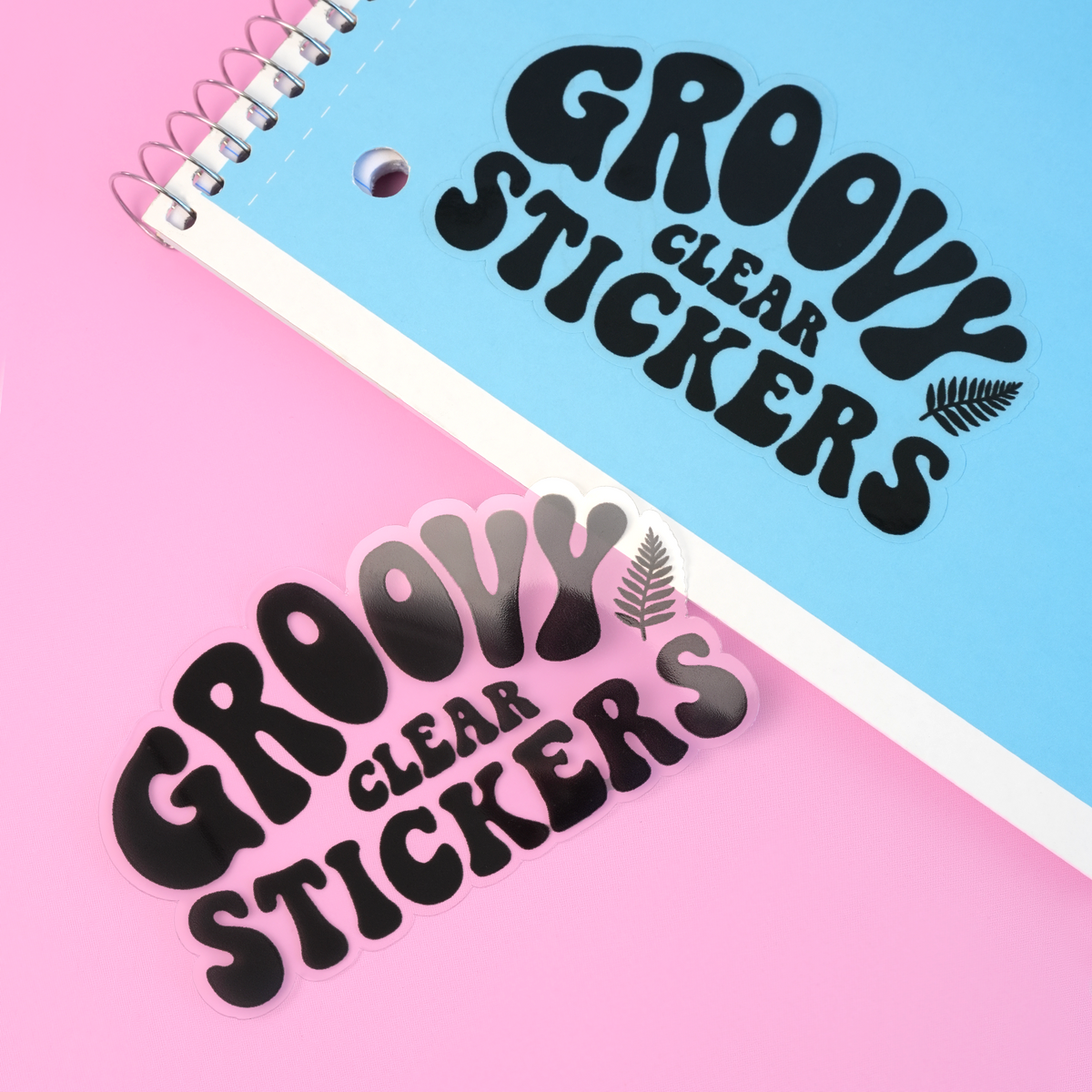 Custom clear stickers with groovy black typography displayed on a spiral notebook and pink surface.