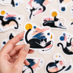 Hand holding a black cat custom art sticker with printed sticker samples in the background