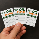 Hand holding custom oil change reminder stickers with mileage, date, and grade service due fields.