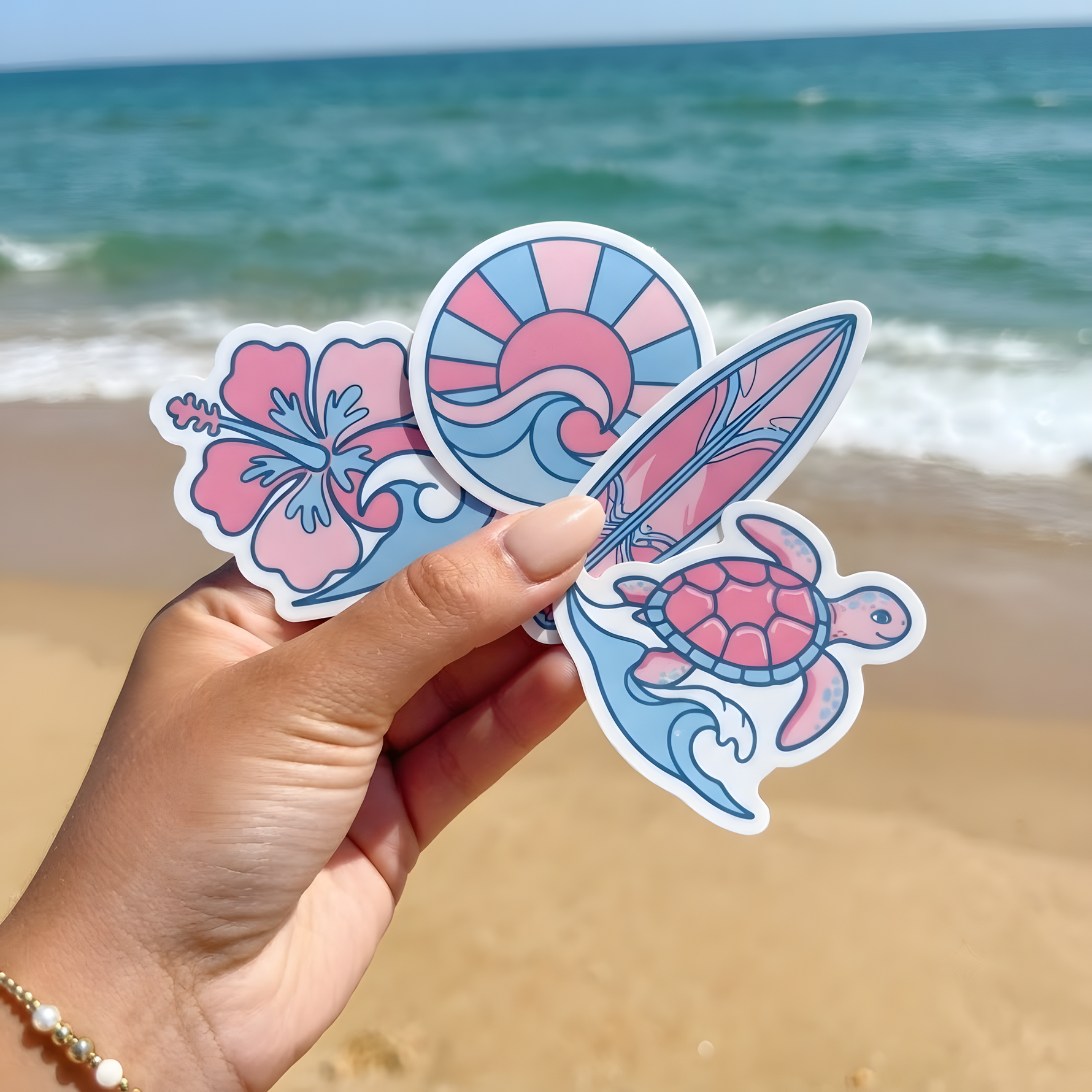 A hand holding pastel-colored sea turtle and surfboard stickers at the beach