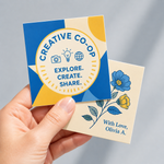 Hand holding two custom square stickers with brand and floral artwork